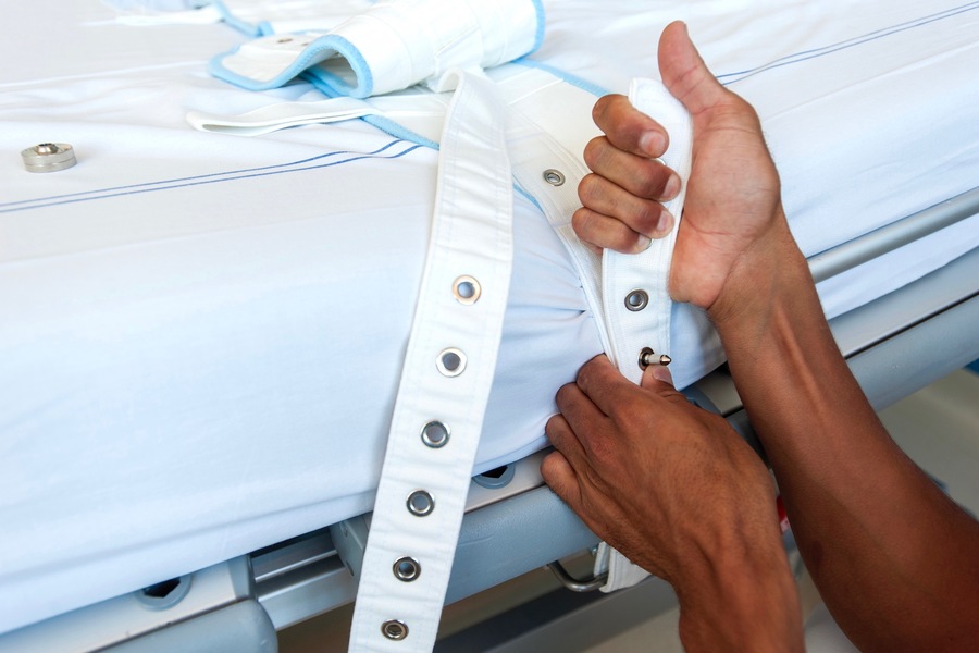 Des contentions sont installées par un professionnel de santé sur le lit d'un patient.
